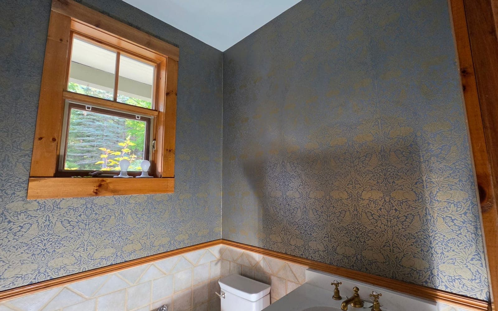 Salle d'eau habillée d'un papier peint à motif floral bleu et or, raccords alignés à l'angle des murs
