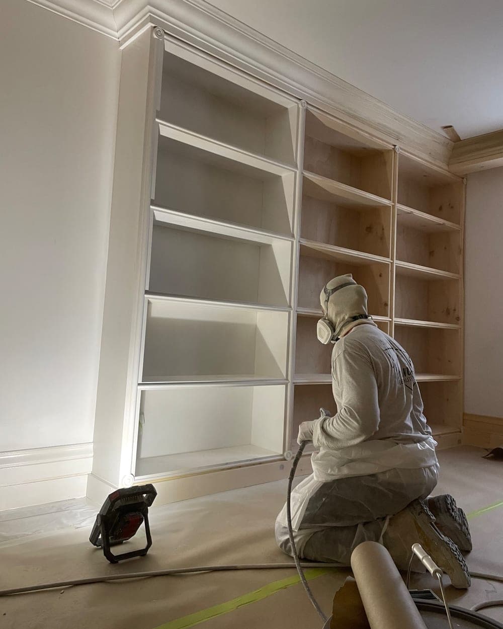 Peintre appliquant la peinture au fusil sur une bibliothèque intégrée, moitié déjà laquée en blanc