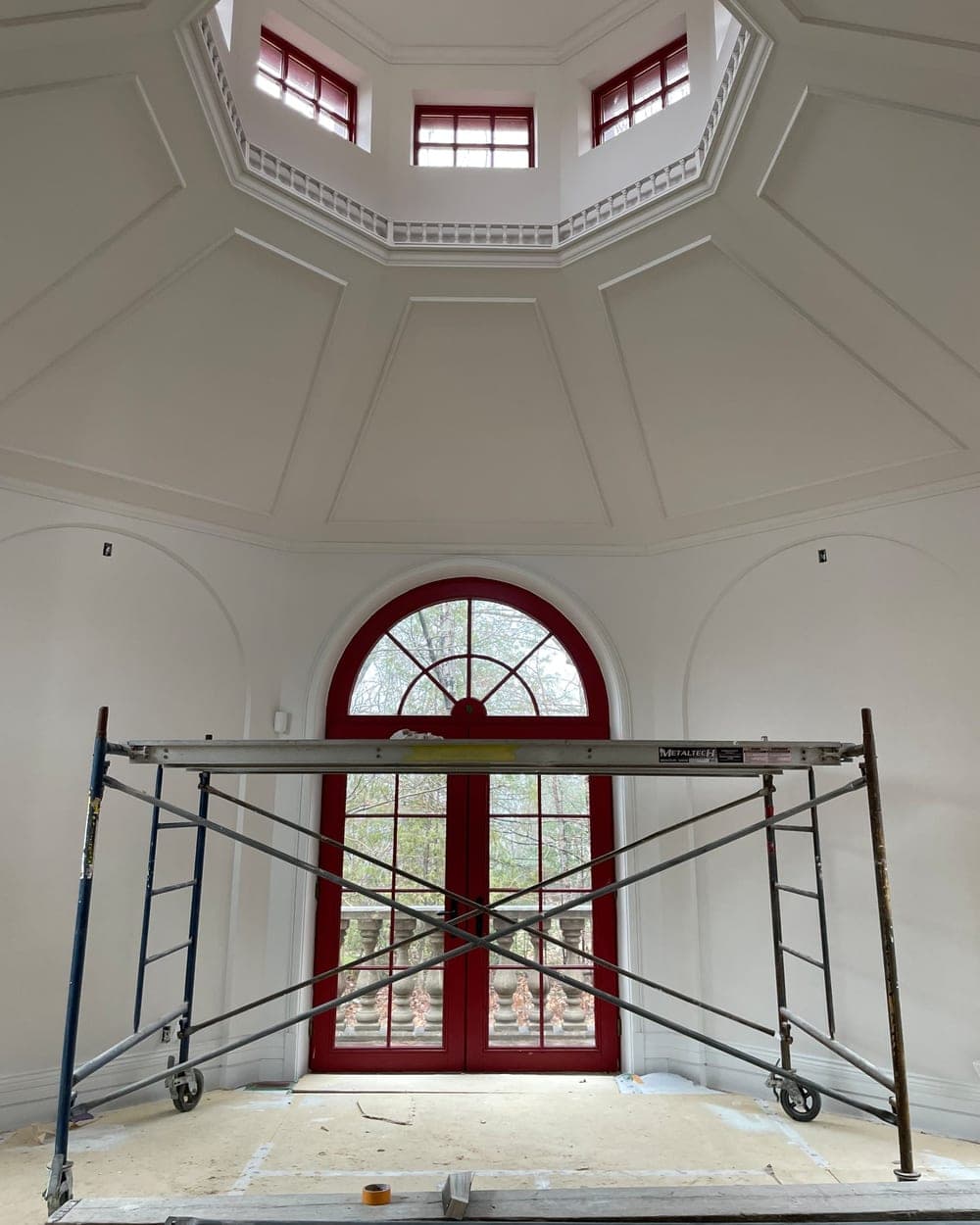 Hall d'entrée octogonal aux moulures blanches et porte cintrée rouge, échafaudage en place